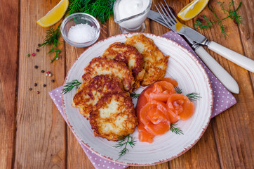 Potato pancakes with sour cream and salmon on a plate on a wooden background