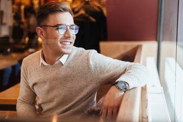 Cheerful young man wearing glasses sitting in cafe