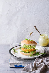Vegetarian hamburger with onion and cheese cutlets, avocado salad, arugula and yogurt sauce in white plate over gray stone texture background. Healthy fast food.