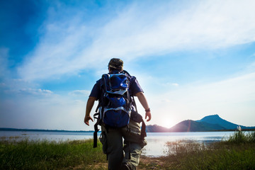 Obraz premium Traveler young man with single backpack,relaxing outdoor with lagoon river mountains on summer vacations and lifestyle concept background