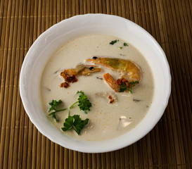 Famous thailand spicy hot soup with red chili peppers, shrimp, lemongrass leaf, ginger root, coconut milk, garlic and parsley. Tom Yum Kung. Asian Dish Cuisine.  Bamboo  napkin on background.