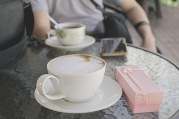 Selective focus white cup of Coffee, latte on the wooden table with pink gift.
