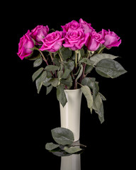 Leaves falling off of old roses in a vase