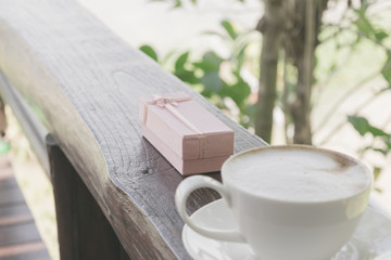 Close up white cup of Coffee, latte on the wooden table with pink gift.
