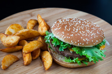 Fresh homemade beef  double cheese burger with cheese, vegetables, tomatoes, salad lettuce, onion, spicy tomato sauce and potato slices on wooden board background. Fast food concept.
