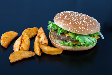 Fresh homemade beef  double cheese burger with cheese, vegetables, tomatoes, salad lettuce, onion, spicy tomato sauce and potato slices on  black wooden table. Fast food concept.
