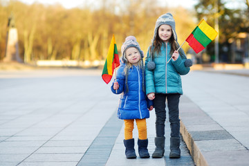 Two adorable little sisters celebrating Lithuanian Independence Day holding tricolor Lithuanian...