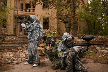 young boys playing paintball. boy aiming a paintball gun. Boy in camouflage clothing. boy in a protective suit. Boy in a protective mask. game of war. war game. Boy shoots a gun.