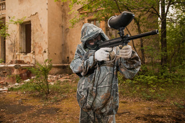 Fototapeta premium young boy playing paintball. boy aiming a paintball gun. Boy in camouflage clothing. boy in a protective suit. Boy in a protective mask. game of war. war game. Boy shoots a gun.