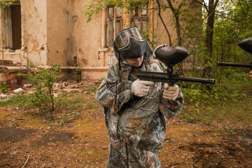 Fototapeta premium young boy playing paintball. boy aiming a paintball gun. Boy in camouflage clothing. boy in a protective suit. Boy in a protective mask. game of war. war game. Boy shoots a gun.