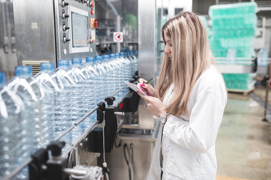Young happy female worker in factory writing notes about water bottles or gallons before shipment. Inspection quality control. 