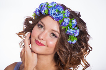 young and beautiful brown-haired woman on a white background in a blue dress with flowers in her hair