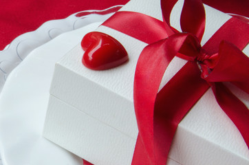 Close up of  white gift box with red ribbon bow and decorative heart. Love romantic background. Valentine´s Day concept.