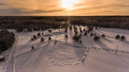 Strong sunset over evening winter forest in countryside. Aerial view. Russian village with paddock
