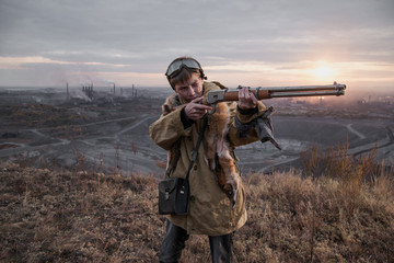 young boy standing on a mountain with a gun. post-apocalyptic world. boy with fox skin on his shoulders. boy aiming a gun. teenager forest hunter. Apocalypse