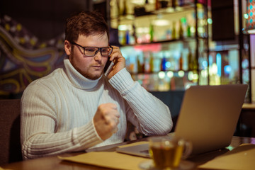 Handsome young man with laptop and cup in a cafe