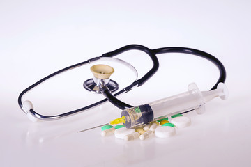 Stethoscope, syringe and pills on a white background