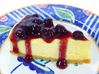 Baked cheesecake with blueberry sauce served on white and blue plate 