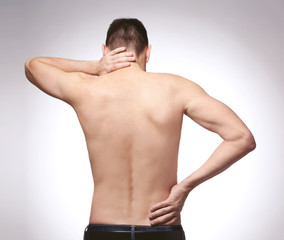 Young man with back pain on light background