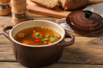 Pot with fresh vegetable soup on wooden background