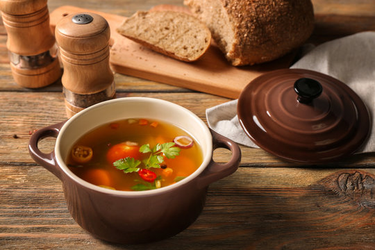 Pot with fresh vegetable soup on wooden background