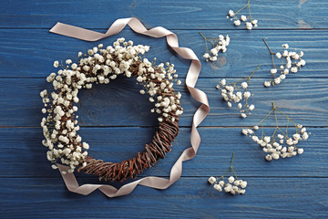 Beautiful floral wreath with satin ribbon on dark wooden background
