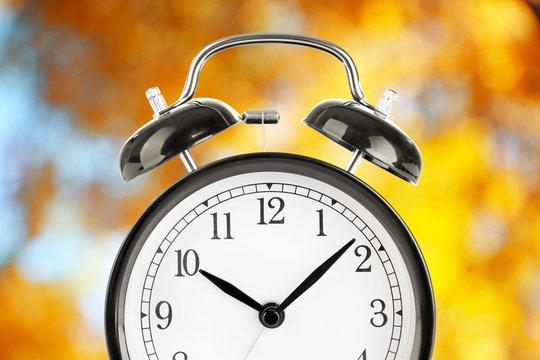 Alarm clock on blurred yellow foliage background. Time change concept
