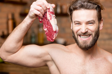 Portrait of a naked muscular man with raw meat on the kitchen