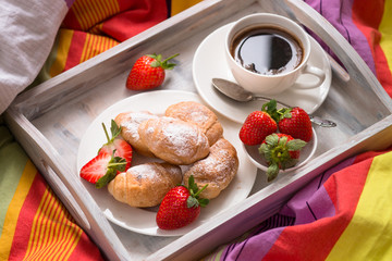 Mini croissants with berries and coffee in wooden tray in a bed.
