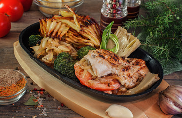 chicken breast stuffed with tomato, garlic and cheese with pickled onions, artichoke, broccoli, fried potatoes in a frying pan on the Board. served on rustic