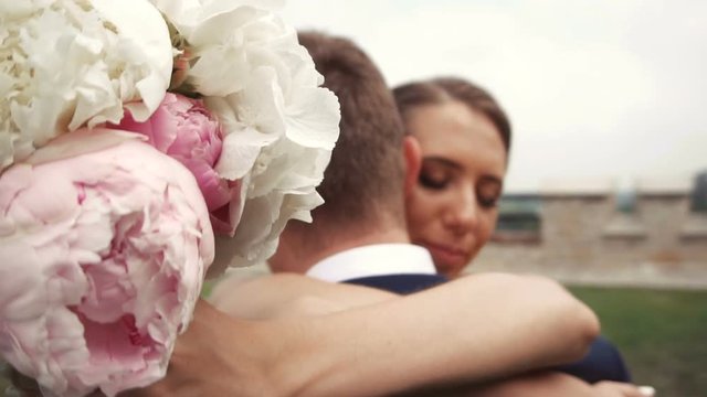 Beautiful young wedding couple embracing in the park with flower bouquet