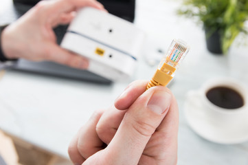 Businessman holds LAN cable over desk with laptop and mobile WiFi