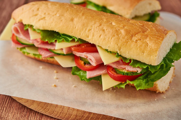 Submarine sandwich with ham, cheese, tomatoes, lettuce, cucumbers and onions on a wooden background