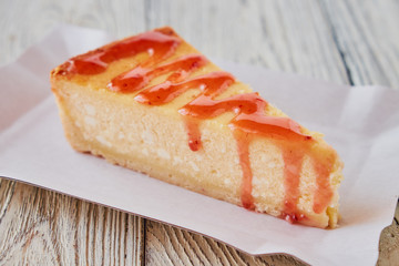 Slice of the New York cheesecake on a white plate on a wooden background .