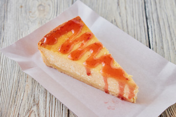 Slice of the New York cheesecake on a white plate on a wooden background .
