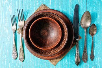 Brown plates with cutlery on rustic wooden table, top view