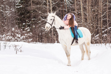 Nice girl and white horse outdoor in snowfall in a winter