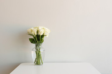 Crème rozen in glazen vaas op witte tafel tegen neutrale muur