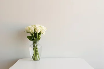 Fotobehang Rozen Crème rozen in glazen vaas op witte tafel tegen neutrale muur