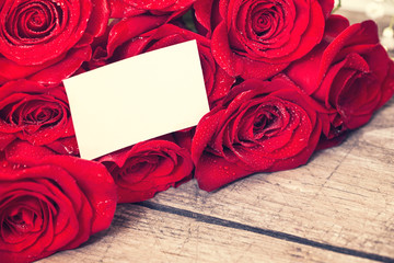 greeting card and red roses on wooden table.