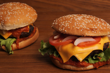 Homemade hamburger with double cheese, tomatoes, onions and grated carrots on a wooden table, unhealthy food. 
