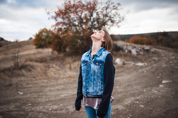 portrait of the attractive, slender, beautiful young Caucasian blonde girl in a jeans jacket. Smiling girl enjoys fine warm sunner weather highly in mountains against the sea