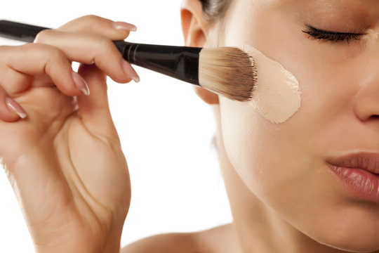 Fototapeta A young woman applied liquid foundation on her face with a brush