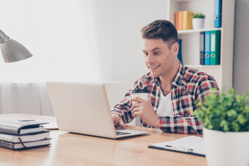 Young happy guy with cup of coffee using laptop