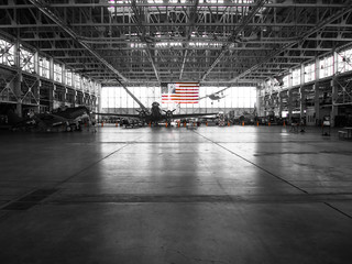The American flag stands out in the background of this black and white photo of an airplane hangar.