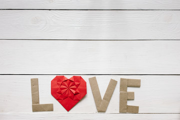 Red origami heart, craft paper folded letters Love inscription on white painted rustic rural barn wood background. Nice Valentines day holiday greeting card, postcard template.