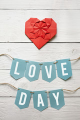 Red origami paper heart on white wooden planks flat lay. Love day lettering. Simple and cozy St. Valentines Day holiday concept.