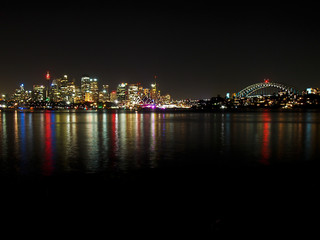 The lights of Sydney reflect in the harbor at night.