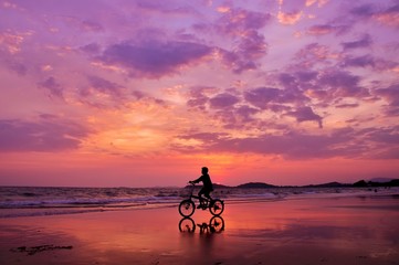 Fototapeta premium Silhouette of boy riding a bicycle on the beach with drametic sky