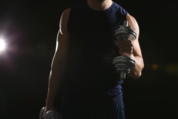 Sporty man doing exercises with dumbbells on black background, closeup